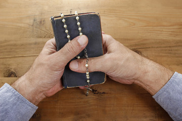 Wall Mural - Hands with rosary over old Holy Bible. Wooden background.