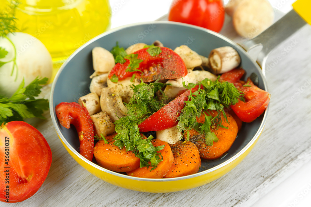 Sliced fresh vegetables in pan on wooden board isolated on