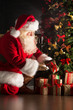 © Milles Studio - Santa putting gifts under Christmas tree in dark room
