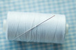 Spool of white thread with sewing needle