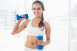 © lightwavemedia - Smiling young brunette holding dumbbells