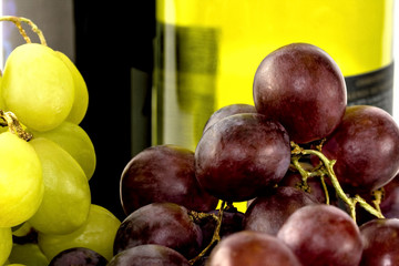 Green and black grapes with two wine bottles