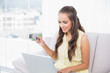 © lightwavemedia - Smiling young brunette using credit card and laptop