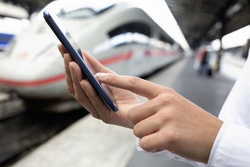 Wall Mural - Close up of hands woman using her cell phone at a station platfo