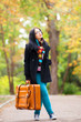 © Masson - Brunette girl holding suitcase at autumn alley in the park