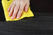 Hand wiping wooden surface with yellow rag