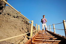 Man Trekking On Wooden Stairs Along A Rocky Path