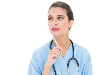 Wall Mural - Thoughtful brown haired nurse in blue scrubs holding a pen