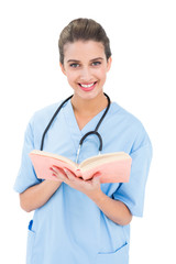 Wall Mural - Happy brown haired nurse in blue scrubs holding a book