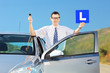 Happy man posing near car, holding L sign and key