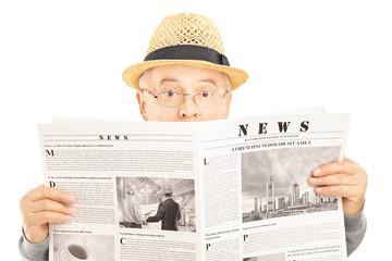 Canvas Print - Scared senior man with glasses hiding behind a newspaper