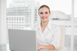 © lightwavemedia - Happy businesswoman using laptop looking at camera