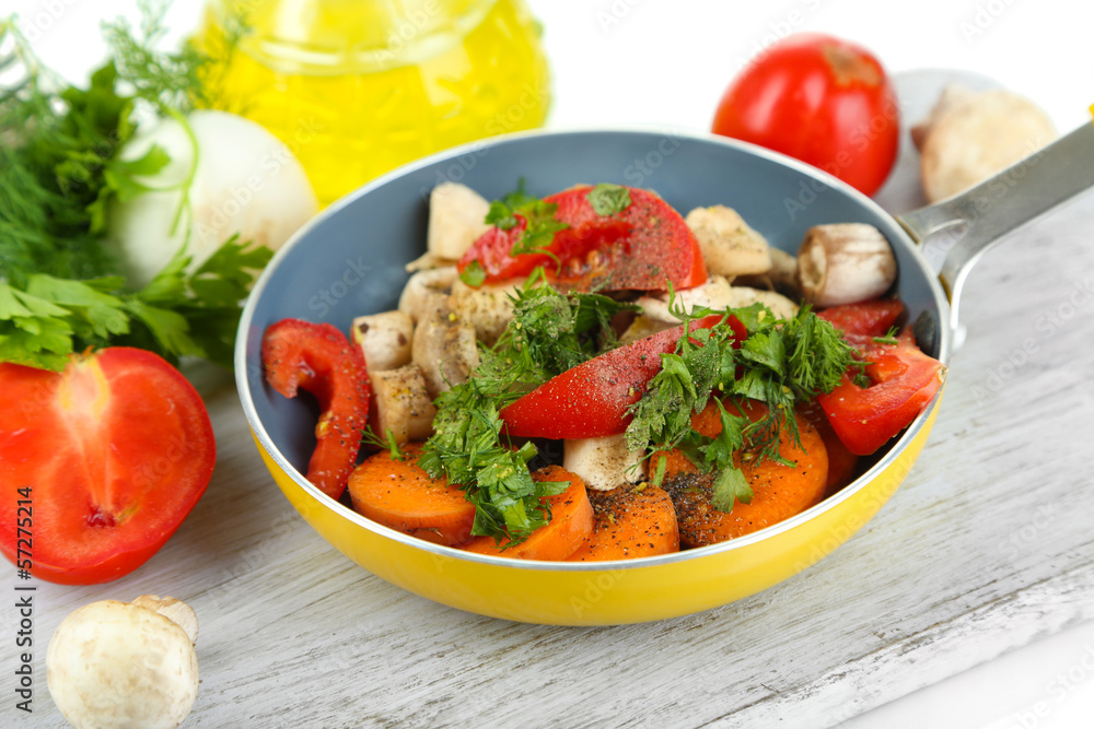 Sliced fresh vegetables in pan on wooden board isolated on