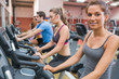 © WavebreakmediaMicro - Smiling woman with other people riding an exercise bike