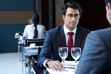 Two smiling business men have dinner at restaurant