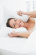 © lightwavemedia - Smiling woman covering ears with pillow in bed