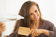 Happy Young Woman Brushing And Blow Drying Hair In Bathroom
