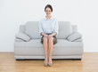 © lightwavemedia - Full length of a smiling well dressed woman sitting on sofa