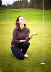 Young woman golf player holding ball looking at cup flag