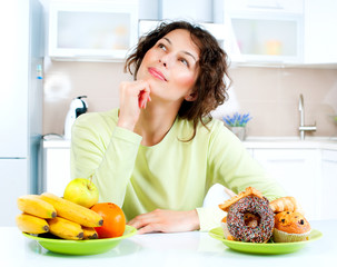 Wall Mural - Dieting concept. Young Woman choosing between Fruits and Sweets