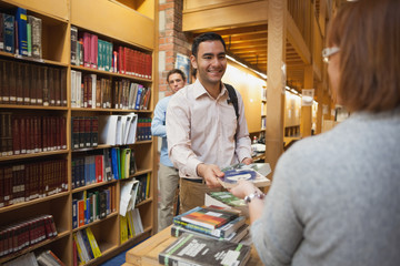 Wall Mural - Mature female librarian handing a book to young man