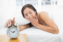 Woman Yawning While Extanding Hand To Alarm Clock