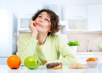 Wall Mural - Dieting concept. Young Woman choosing between Fruits and Sweets