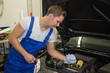 Mechanic in garage checking motor oil level at a car