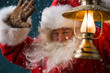 Santa Claus is holding a shining lantern while sneaking to his h