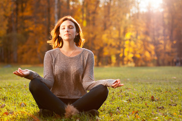 Beautiful young girl meditating in autumn park