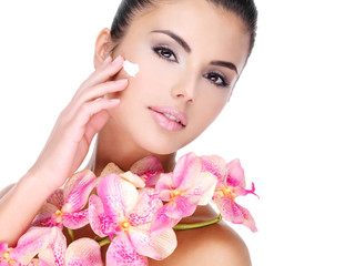 Wall Mural - woman applying cosmetic cream on face with pink flowers on body