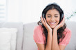 © lightwavemedia - Content cute brunette sitting on couch listening to music with c