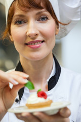 Wall Mural - Gorgeous head chef putting mint leaf on little cake on plate