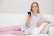 © lightwavemedia - Happy casual blonde relaxing on couch holding smartphone