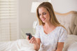 © lightwavemedia - Natural content woman sitting in bed holding smartphone
