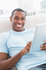 Casual smiling young Afro man using digital tablet on sofa