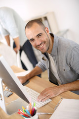 Wall Mural - Cheerful guy sitting in front of desktop computer