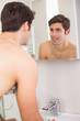 © lightwavemedia - Rear view of a young smiling at self in bathroom mirror