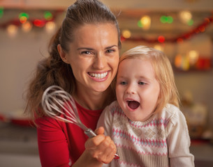 Portrait of happy mother and surprised baby looking on whisk