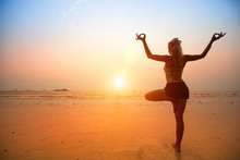 Young Woman Practicing Yoga On The Beach At Sunset.
