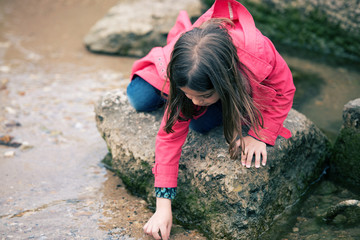 Wall Mural - pretty little girl playing on a rock at the water's edge