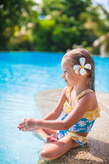 Wall Mural - Adorable girl with flower behind her ear sits near swimming pool