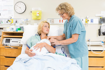Fototapete - Smiling Nurse Assisting Woman In Breast Feeding Baby In Hospital