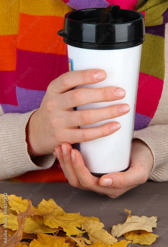Hot drink in plastic glass in hands on wooden table close up