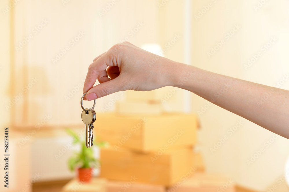 Female hand with keys ob stack of cartons background: moving