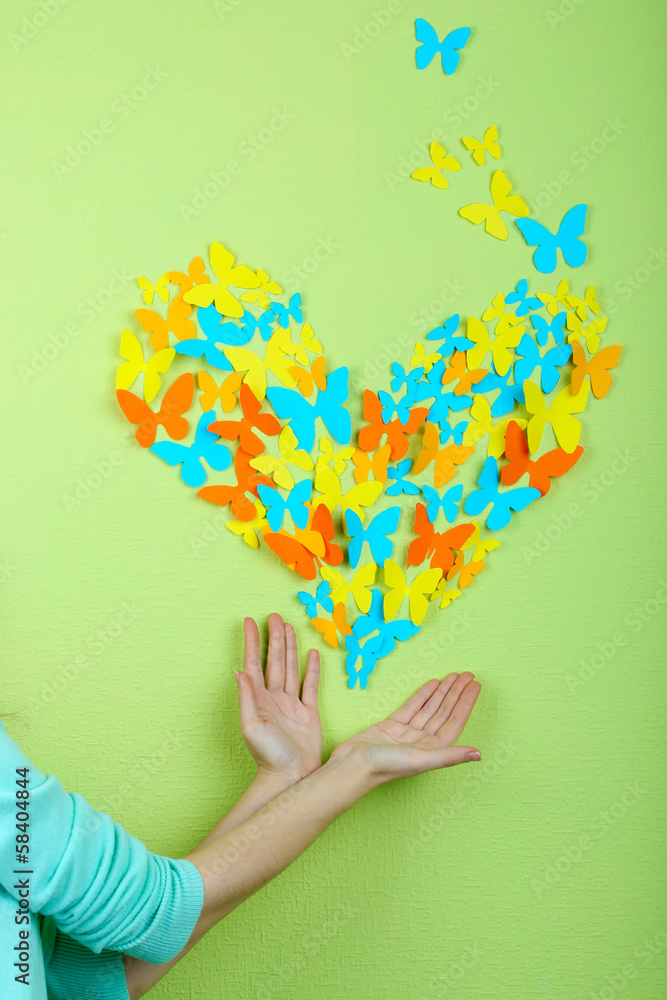 Paper butterflies on hands on green wall background