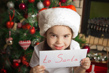 Happy little girl with letter to Santa near christmas tree