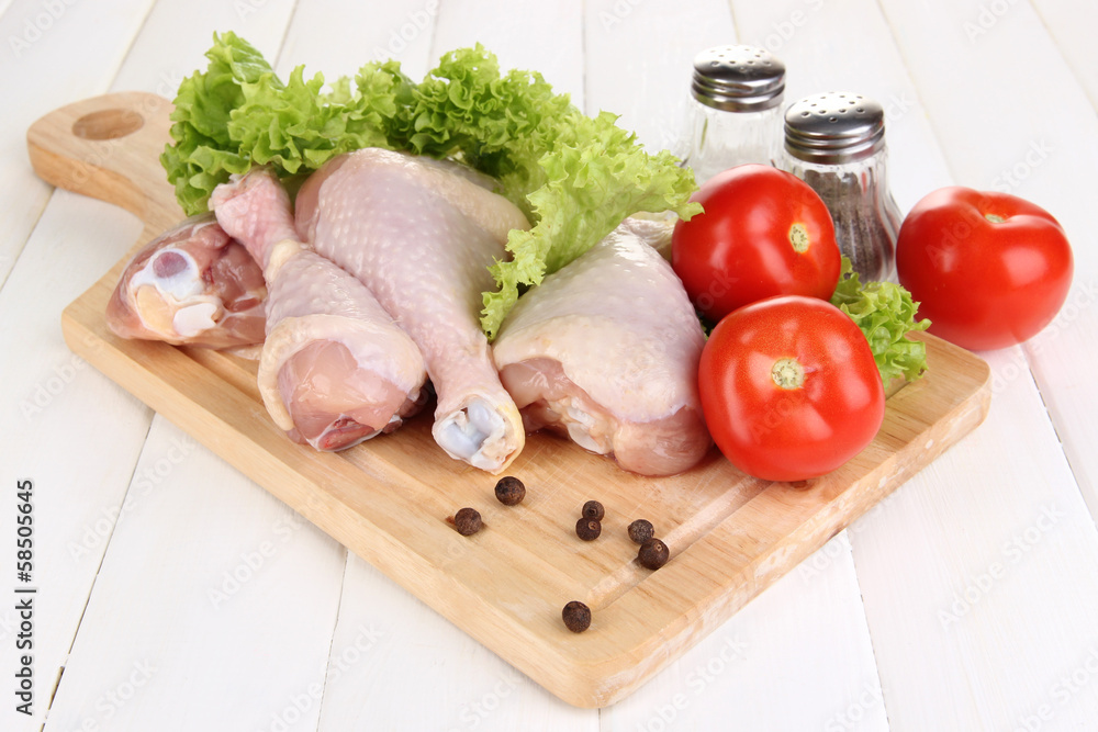 Raw chicken legs on wooden board on wooden table