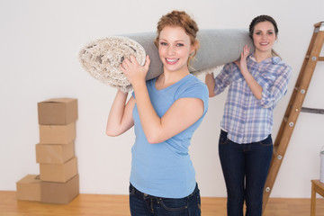 Smiling friends carrying rolled rug after moving in a house