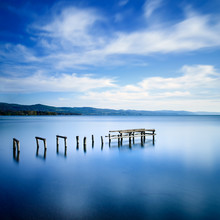 Wooden Pier Or Jetty Remains On A Blue Lake. Long Exposure.